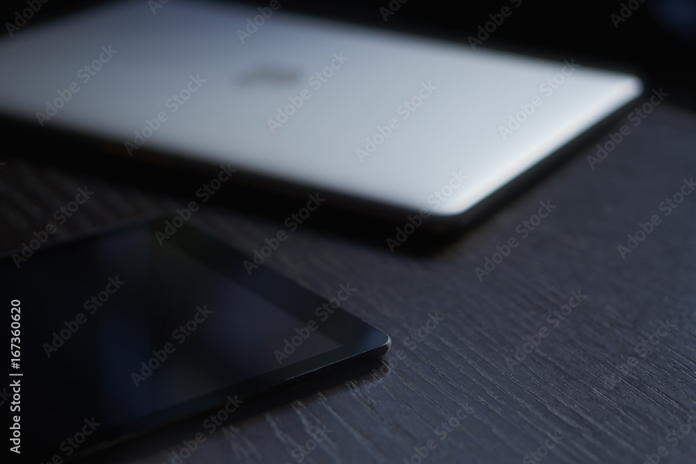 Close-up of a tablet lying on a dark desk next to the laptop Close-up of a tablet lying on a dark desk next to the laptop