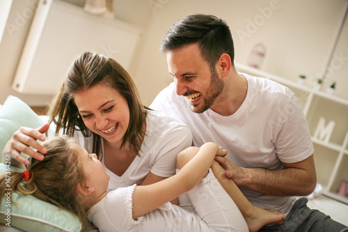 Parents having fun with their little daughter on bed. Family spending time at the morning. © liderina