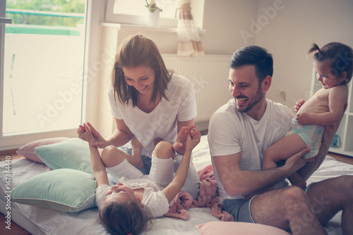 Family spending free time at home. Cheerful family having fun with their daughters on the bed.