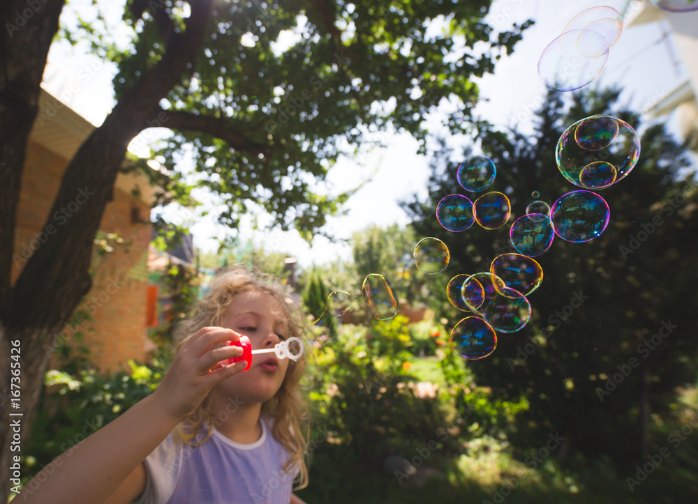 Cute little girl is blowing a soap bubbles.