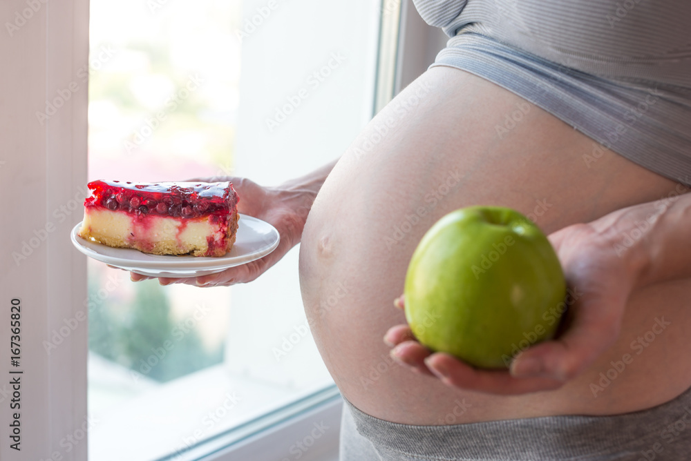 © Artem - Pregnant woman belly holding a plate with junk and healthy food. Concept choice of diet during pregnancy