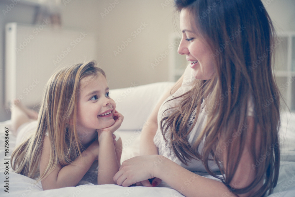 Mother with her cute little daughter lying  on bed.