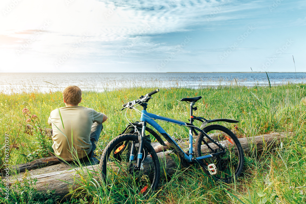 Obraz premium young man sitting on the beach with the bike