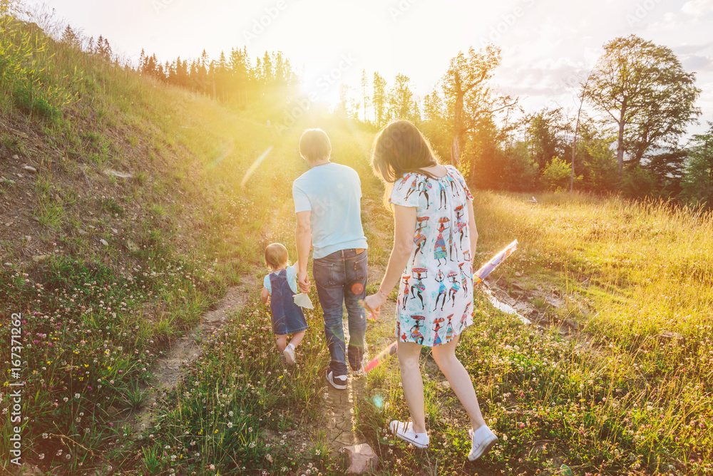 Fototapeta premium mother and father holding daughter hands and walking by mountains