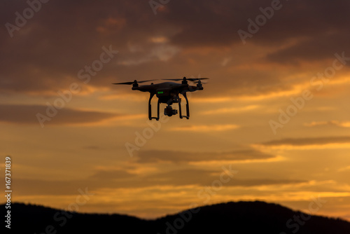 Drone silhouette flying in sunset landscape © ba11istic