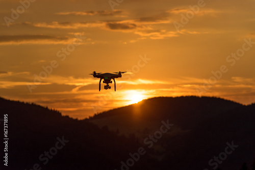 Drone silhouette flying in sunset landscape © ba11istic