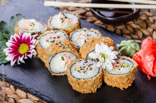 Fototapeta Hot fried Sushi rolls and maki set with Crab Meat, cream cheese, avocado and wasabi on black stone on bamboo mat, selective focus