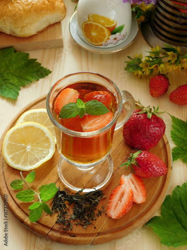 Spicy tea with strawberries illuminated by the sun rays on a wooden background