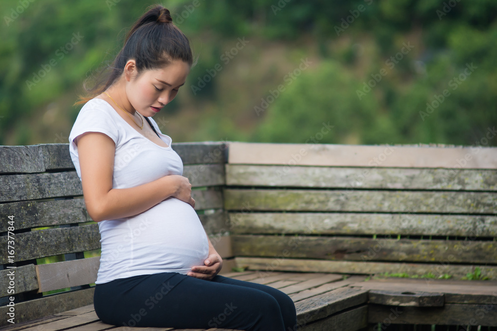 Young beautiful pregnant woman hands holding belly and sitting on wooden chair at mountain. Young beautiful pregnant woman hands holding belly and sitting on wooden chair at mountain.