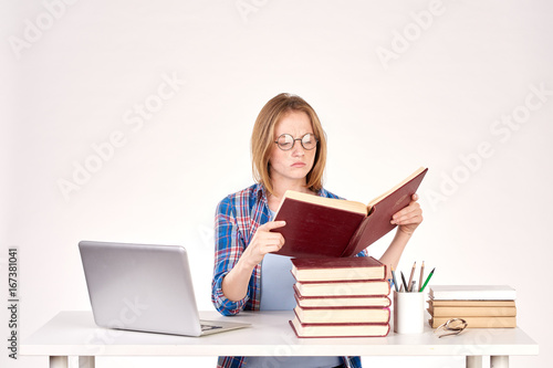 Beautiful teenage schoolgirl sitting at desk with stack of books on it