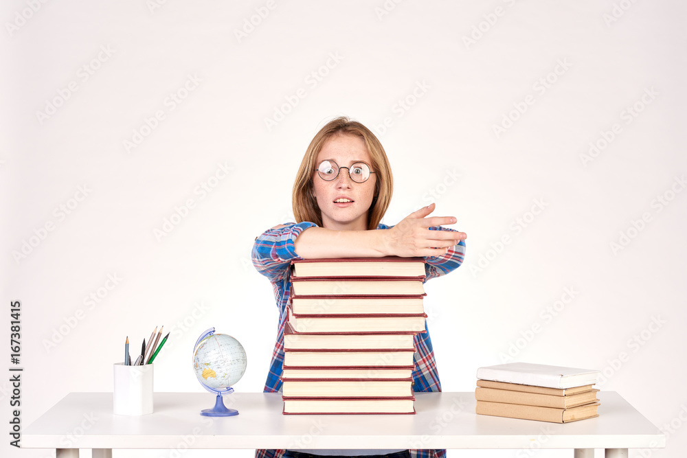 Beautiful teenage schoolgirl sitting at desk with stack of books on it Beautiful teenage schoolgirl sitting at desk with stack of books on it