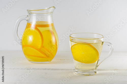 Lemonade from oranges in a glass pitcher and mugs on a light background.