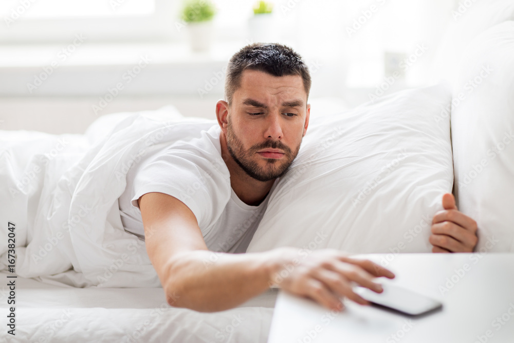 young man reaching for smartphone in bed young man reaching for smartphone in bed