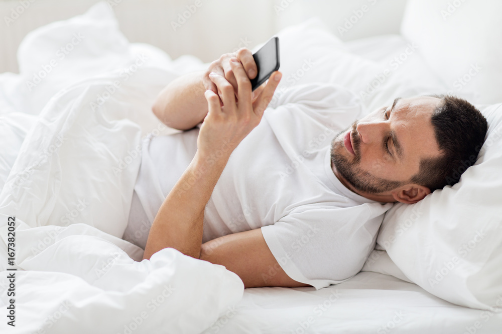 young man with smartphone in bed in morning young man with smartphone in bed in morning