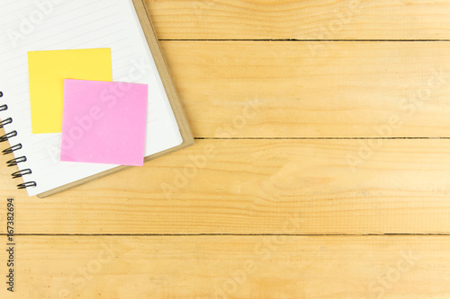 Pink and yellow post it on blank notepad on wooden table