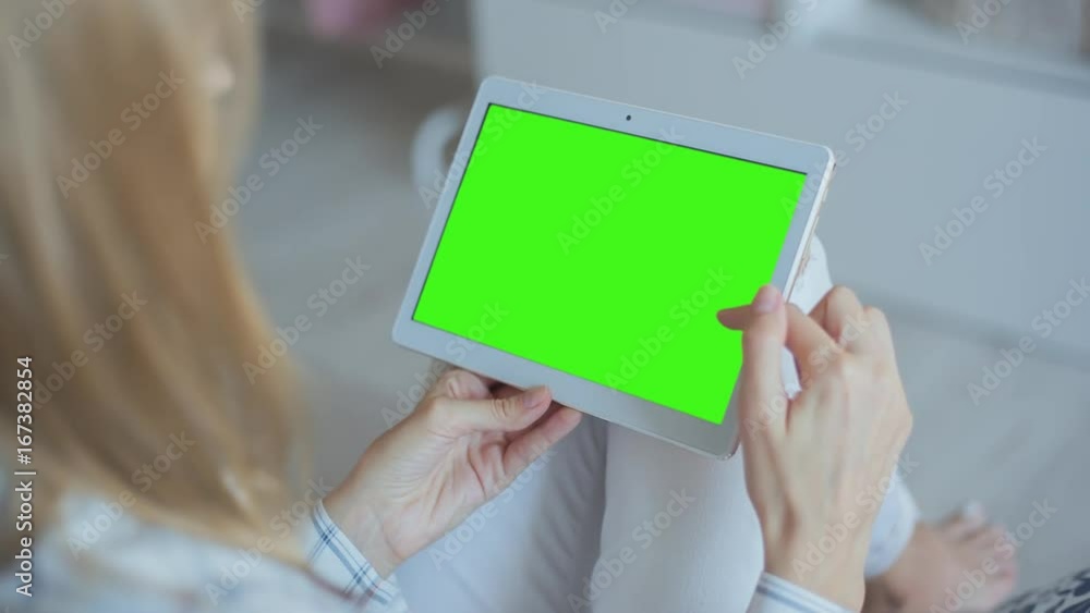Young Woman in white jeans sitting on couch uses Tablet PC with pre-keyed green screen. Few types of gestures - scrolling up and down, tapping, zoom in and out. Perfect for screen compositing Young Woman in white jeans sitting on couch uses Tablet PC with pre-keyed green screen. Few types of gestures - scrolling up and down, tapping, zoom in and out. Perfect for screen compositing