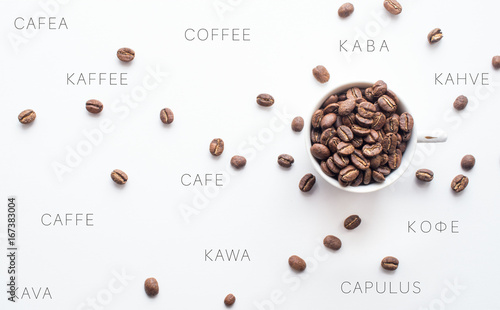 Bright coffee beans in a cup and spread over a light background with coffee spelled in different languages, representing an international component to coffee consumption. 