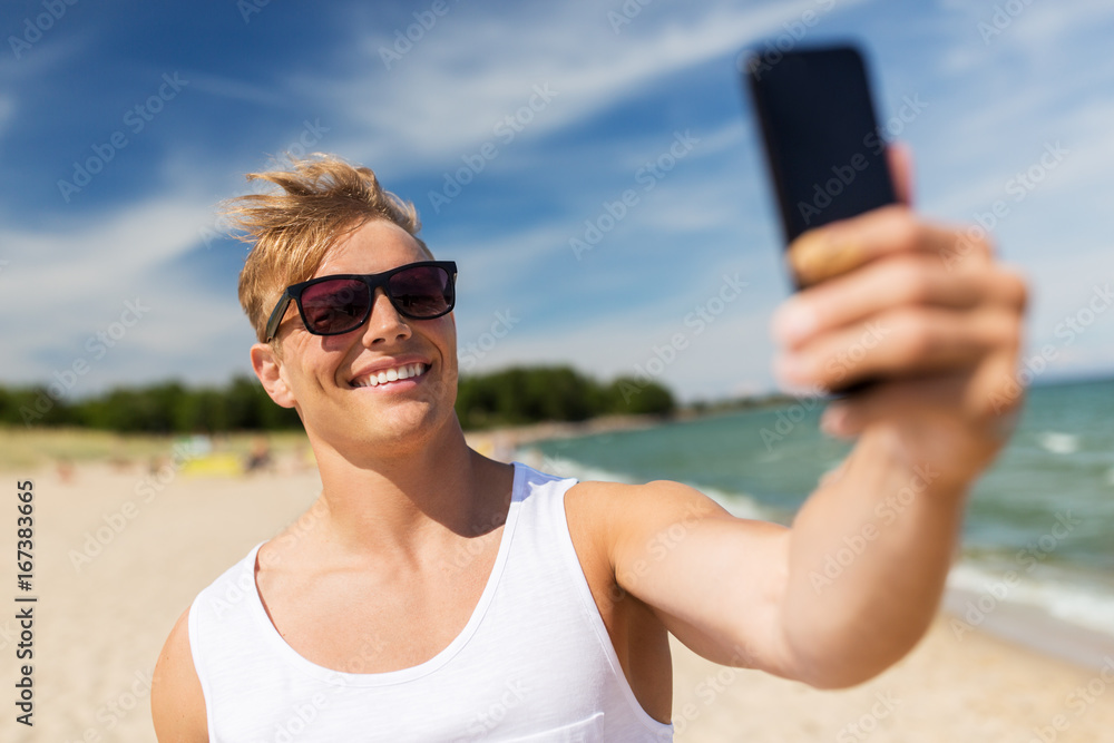 man with smartphone taking selfie on summer beach