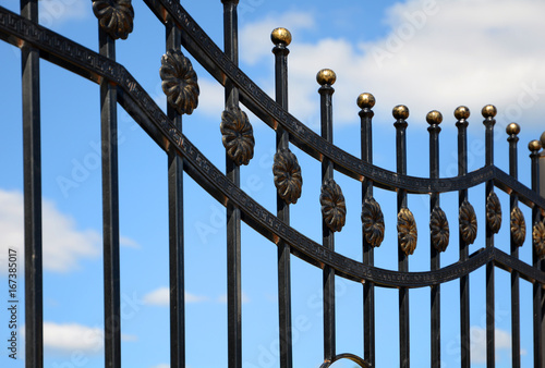 Beautiful wrought fence against blue sky. Image of a decorative cast iron fence. Metal fence close up. 