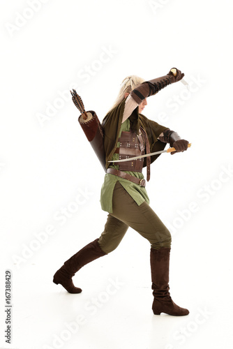 full length portrait of a blonde girl wearing green and brown medieval costume, holding a bow and arrow. isolated on white background. photo