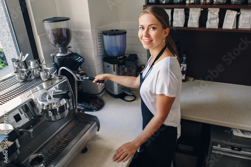 Portrait of Caucasian barista woman girl with filter holder grinding  fresh roasted coffee beans. Preparing coffee in coffee shop cafe.