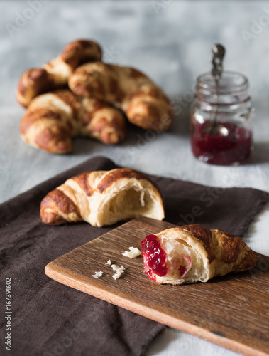 Croissant auf dunklem Holzbrett mit Erdbeermarmelade zum Frühstück auf hellem Untergrun