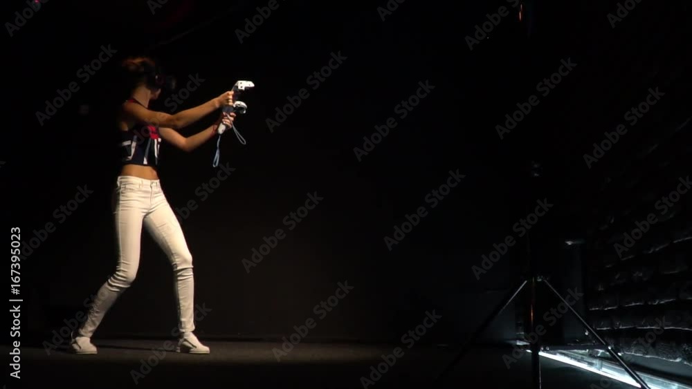 A girl with virtual reality glasses and two joysticks in her hands plays a game in a dark room A girl with virtual reality glasses and two joysticks in her hands plays a game in a dark room