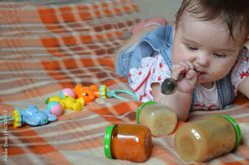 cute baby playing with silver spoon, baby food, baby mashed in a glass jar with photo