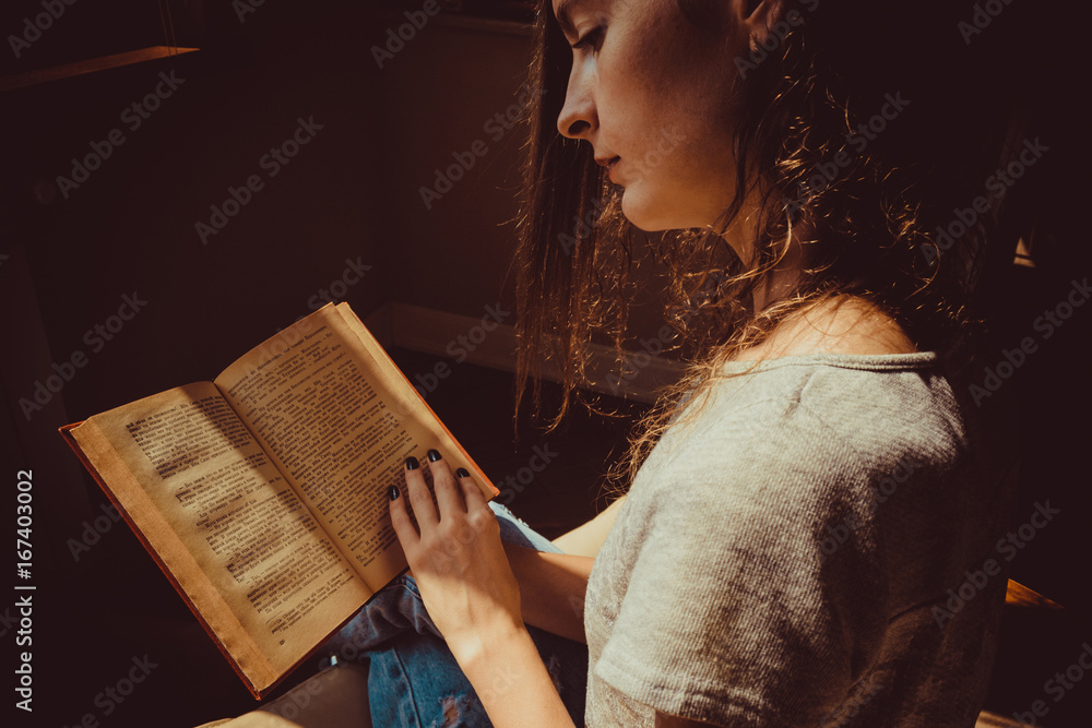 Foto de Spending free time by reading books. Girl reads avidly old  interesting paper book. Natural light. Warm atmosphere. Knowledge, learning  and education concept. Woman bookwarm. Close-up. Read more. do Stock