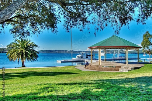 Canvas Print Lush green grassy waterfront park with a quaint little old Bandstand