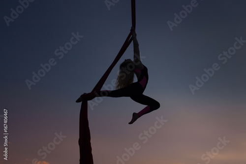 Silhouette of a woman acrobat during a show on canvases in the air.