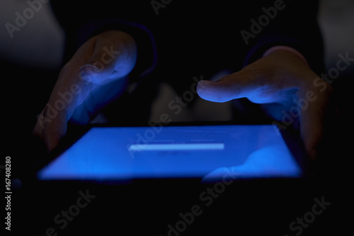 Close-up of a girl working on a tablet with a blue screen in dark illumination on a blurred background