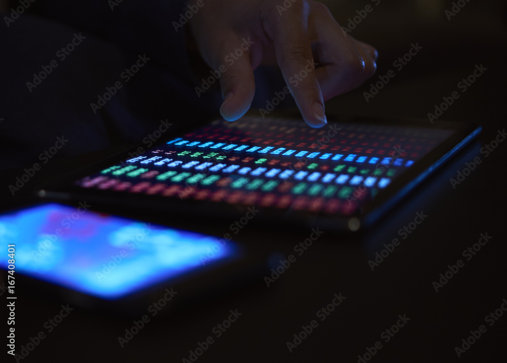 Close-up of the action on the screen of the tablet with dark lighting on a background blurred phone on the screen of which the girl is looking at the exchange rate Close-up of the action on the screen of the tablet with dark lighting on a background blurred phone on the screen of which the girl is looking at the exchange rate