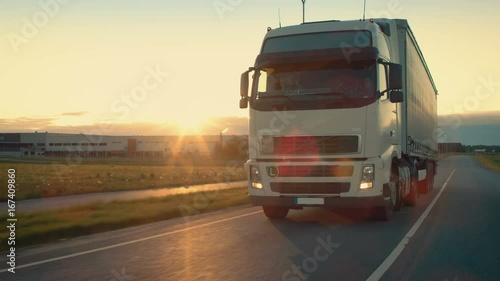 Front-View Camera Follows Semi-Truck with Cargo Trailer Driving on a Highway. He's Speeding Through Industrial Warehouse Area with Sunset in the Background. Shot on RED EPIC-W 8K Helium Cinema Camera.