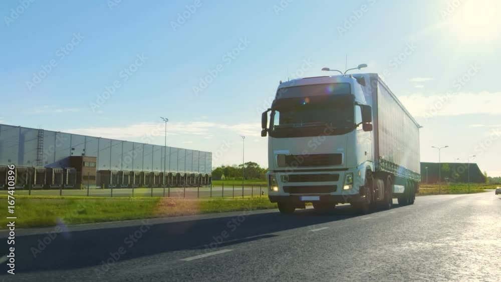 Big White Semi Truck with Cargo Trailer Moves on the Industrial Area Empty Road With Sun Shining in the Background. Shot on RED EPIC-W 8K Helium Cinema Camera. Big White Semi Truck with Cargo Trailer Moves on the Industrial Area Empty Road With Sun Shining in the Background. Shot on RED EPIC-W 8K Helium Cinema Camera.