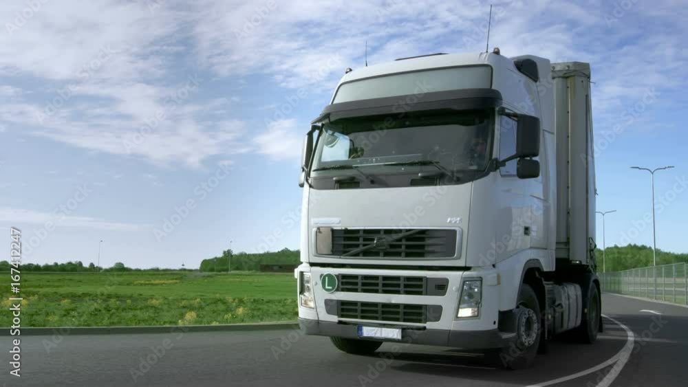 Frontal View of Speeding White Semi Truck with Cargo Trailer Drives on the Highway with Fields and Industrial Warehouses in the Background. Shot on RED EPIC-W 8K Helium Cinema Camera. Frontal View of Speeding White Semi Truck with Cargo Trailer Drives on the Highway with Fields and Industrial Warehouses in the Background. Shot on RED EPIC-W 8K Helium Cinema Camera.