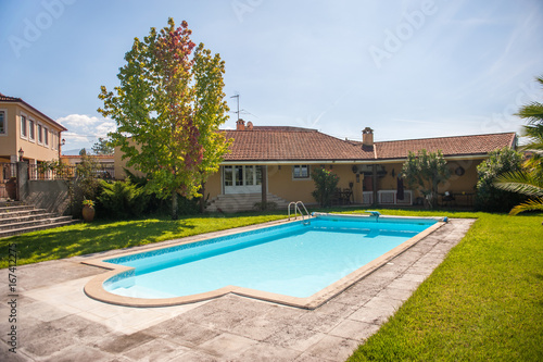 View on a luxury villa and a bright blue pool on a lawn. Shot on a hot summer sunny day with clear sky.