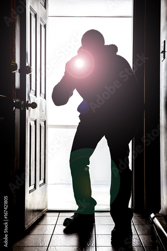 Man crouching at door, in silhouette with flashlight