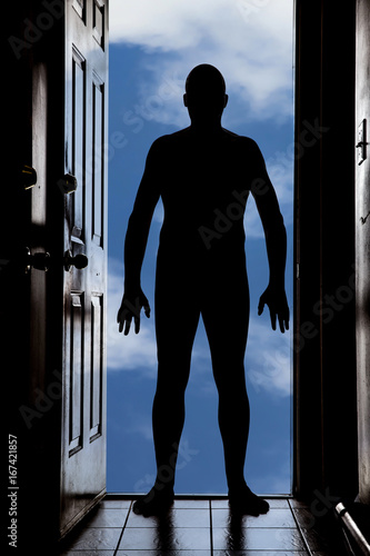 Naked man at door in silhouette with blue sky background