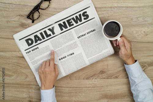 Businessman reading newspapers and holding a cup of coffee on wooden desk.