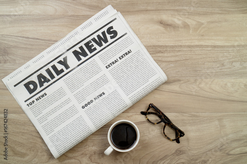 Newspaper on wooden desk with coffee and eyeglasses.
