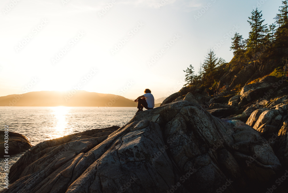 Man sitting on rocks near beach while sunset