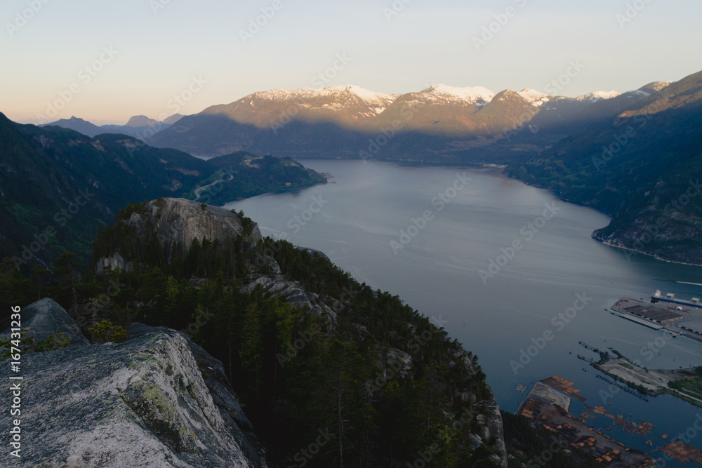 Man in sleeping bag on the top of mountains above lake while sunrise