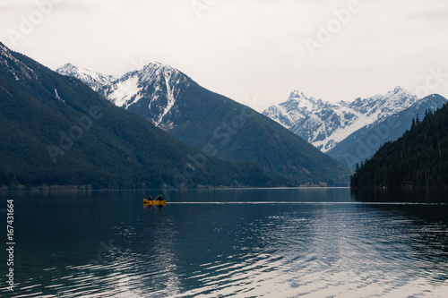 Cloudy landscape with canoe on lake and snow covered mountains © Martin Hossa