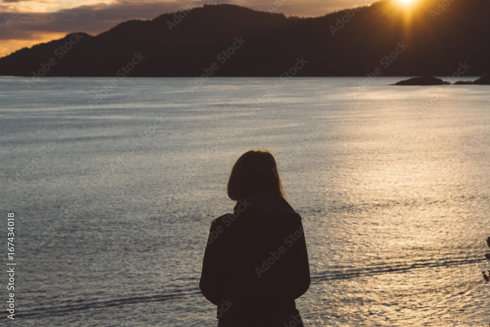 Fototapeta premium Silhouette of woman on coast with ocean and mountains while sunset