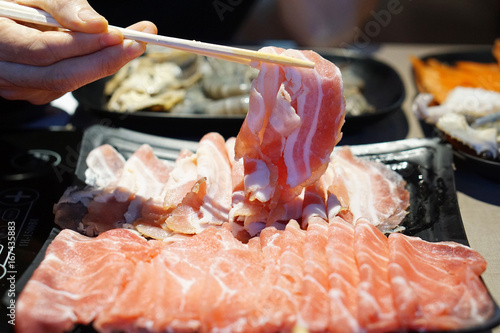 Hand holding raw pork using chopsticks for Japanese hot pot also known as Shabu Shabu or Sukiyaki is Japanese style. photo