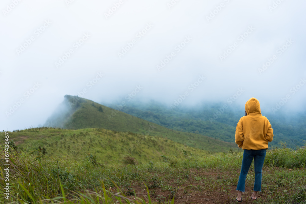 Alone Girl with yellow overcoat and blue jeans has looking for way to the mountain in the heavy mist and cloudy.