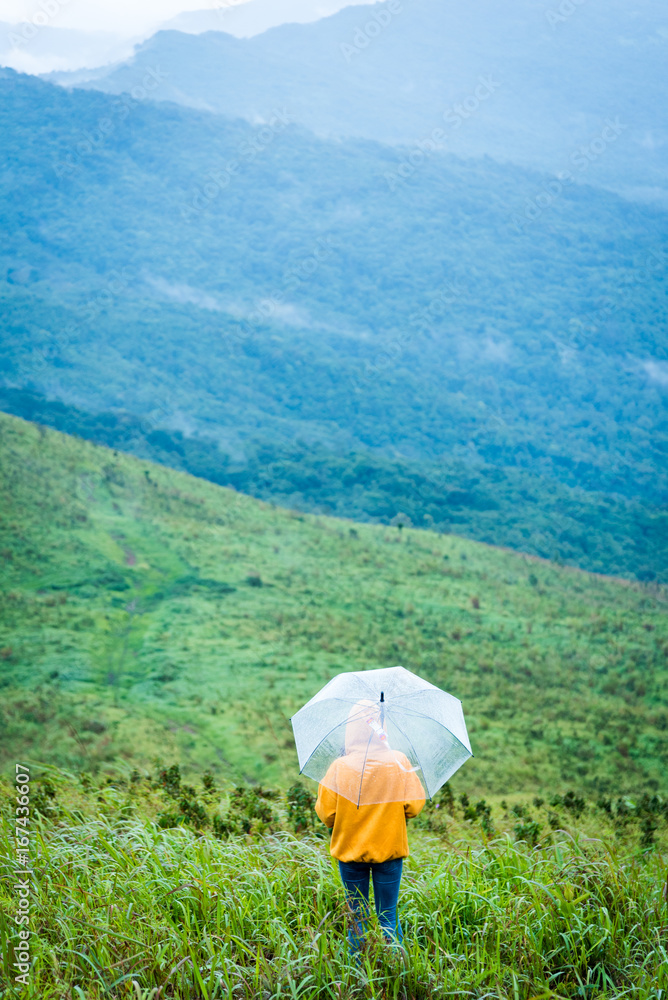 Fototapeta premium Alone female hiker holding umbrella and relaxing with big mountain and heavy mist under the cloudy sky.
