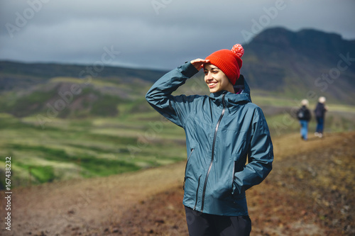 Girl in warm clothing gesturing and observing surroundings on background of mountains of Iceland. 