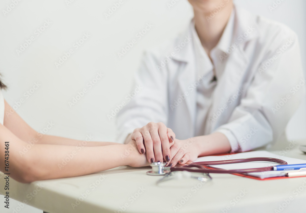 Fototapeta premium Hand of doctor reassuring her female patient in the consulting room.
